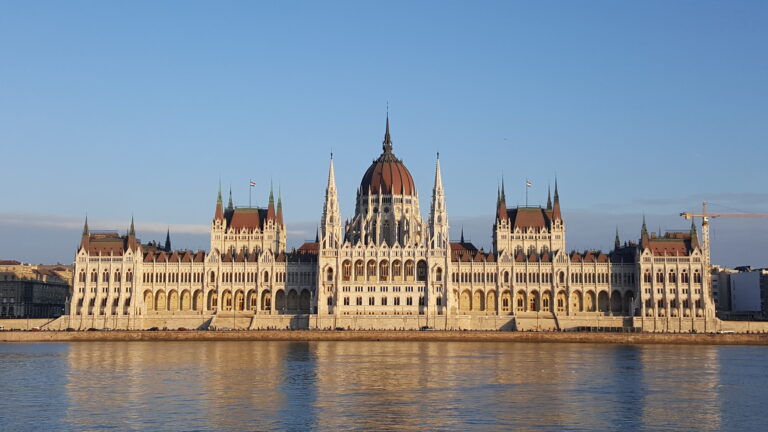 Majestatyczny parlament węgierski w Budapeszcie nad brzegiem Dunaju w złotym świetle słonecznym z charakterystyczną czerwoną kopułą