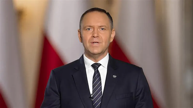 Karol Nawrocki przemawia na tle biało-czerwonych flag.